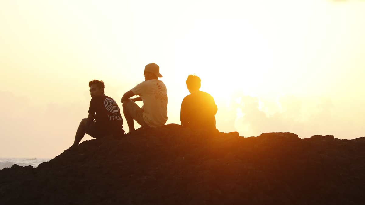 three surfers sitting on a bluff looking at the sunset