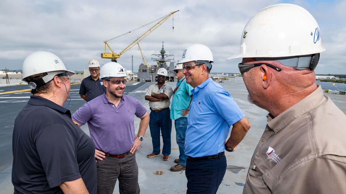 Chris Kastner with colleagues in hard hats at a shipbuilding site